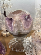 Load image into Gallery viewer, Rainbow amethyst geode sphere on crystal stand showing purple crystal formations on both sides with cream druzy center cavity