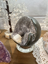 Load image into Gallery viewer, Angled view of hand-polished Brazilian amethyst geode sphere revealing grey and lavender crystal formations with distinctive white calcite crystal