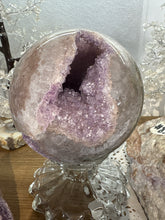 Load image into Gallery viewer, Multi-cavity rainbow amethyst geode sphere displaying two distinct purple amethyst crystal openings with translucent polished exterior