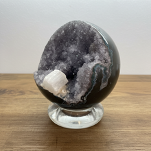 Load image into Gallery viewer, Angled view of hand-polished Brazilian amethyst geode sphere revealing grey and lavender crystal formations with distinctive white calcite crystal