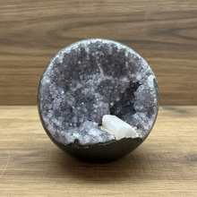 Load image into Gallery viewer, Hand-polished Brazilian amethyst geode sphere on crystal stand showing grey and lavender crystal druzy cavity with white calcite crystal inclusion