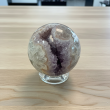 Load image into Gallery viewer, Top-down view of hand-polished rainbow amethyst geode sphere revealing deep purple crystal cavity with sparkling druzy formations