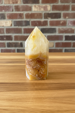Load image into Gallery viewer, Polished citrine tower with natural druzy cavity displaying translucent pale yellow to golden body and sparkling golden-brown crystals on light wood surface with brick background