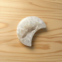 Load image into Gallery viewer, Brazilian agate moon geode carving with translucent white exterior and cream-yellow druzy crystal center displayed on wood table, front view showing crescent shape