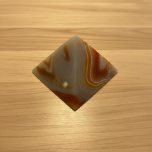 Load image into Gallery viewer, Angled view of Brazilian agate pyramid with warm orange, cream, and grey flowing banding across the polished surface, 7cm base x 5cm height