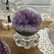 Load image into Gallery viewer, Hand-polished Brazilian amethyst geode sphere on crystal stand showing purple and lavender crystal druzy cavity with smooth dark polished exterior