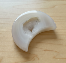 Load image into Gallery viewer, Brazilian agate moon geode carving with milky white exterior and sparkling druzy crystal center displayed on wood table, front view showing crescent shape