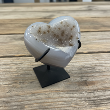 Load image into Gallery viewer, Uruguay agate heart geode displaying translucent layers and golden-brown crystal formation on display stand, angled view