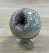 Load image into Gallery viewer, Side profile of hand-polished rainbow amethyst geode sphere showing through-cavity design with purple amethyst crystals
