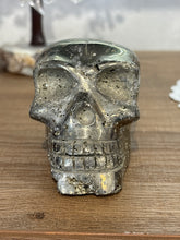Load image into Gallery viewer, Hand-carved pyrite skull from Peru showing side angle with translucent golden-grey tones and black mineral inclusions on light wood surface

