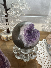 Load image into Gallery viewer, Front view of hand-polished Brazilian amethyst geode sphere displaying purple crystal cavity with darker interior and lighter lavender rim crystals
