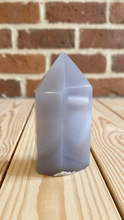 Load image into Gallery viewer, Upright view of white agate tower showing smooth polished finish and elegant translucent milky white coloring on wood surface with brick background
