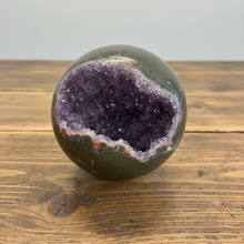 Load image into Gallery viewer, Front view of hand-polished amethyst geode sphere displaying purple and lavender amethyst crystal cavity with darker interior crystals

