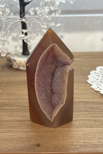 Load image into Gallery viewer, Polished Brazilian agate geode tower with natural druzy-lined cavity displaying rich orange-brown tones on mid-tone wood surface
