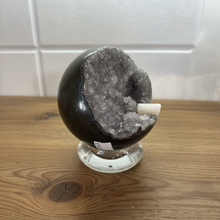 Load image into Gallery viewer, Side view of hand-polished Brazilian amethyst geode sphere displaying grey amethyst crystals and natural white calcite with smooth dark polished exterior
