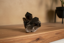 Load image into Gallery viewer, Thunder Bay smokey quartz crystal tower from Brazil showing dramatic vertical formation with dark charcoal points on mid-tone wood mantle, 9x6x6cm premium specimen
