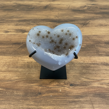 Load image into Gallery viewer, Uruguay agate heart geode with translucent white exterior and golden-brown druzy crystal center on black display stand, front view
