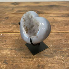 Load image into Gallery viewer, Uruguay agate heart specimen showing natural grey banding and sparkling golden druzy crystals on black stand, side view
